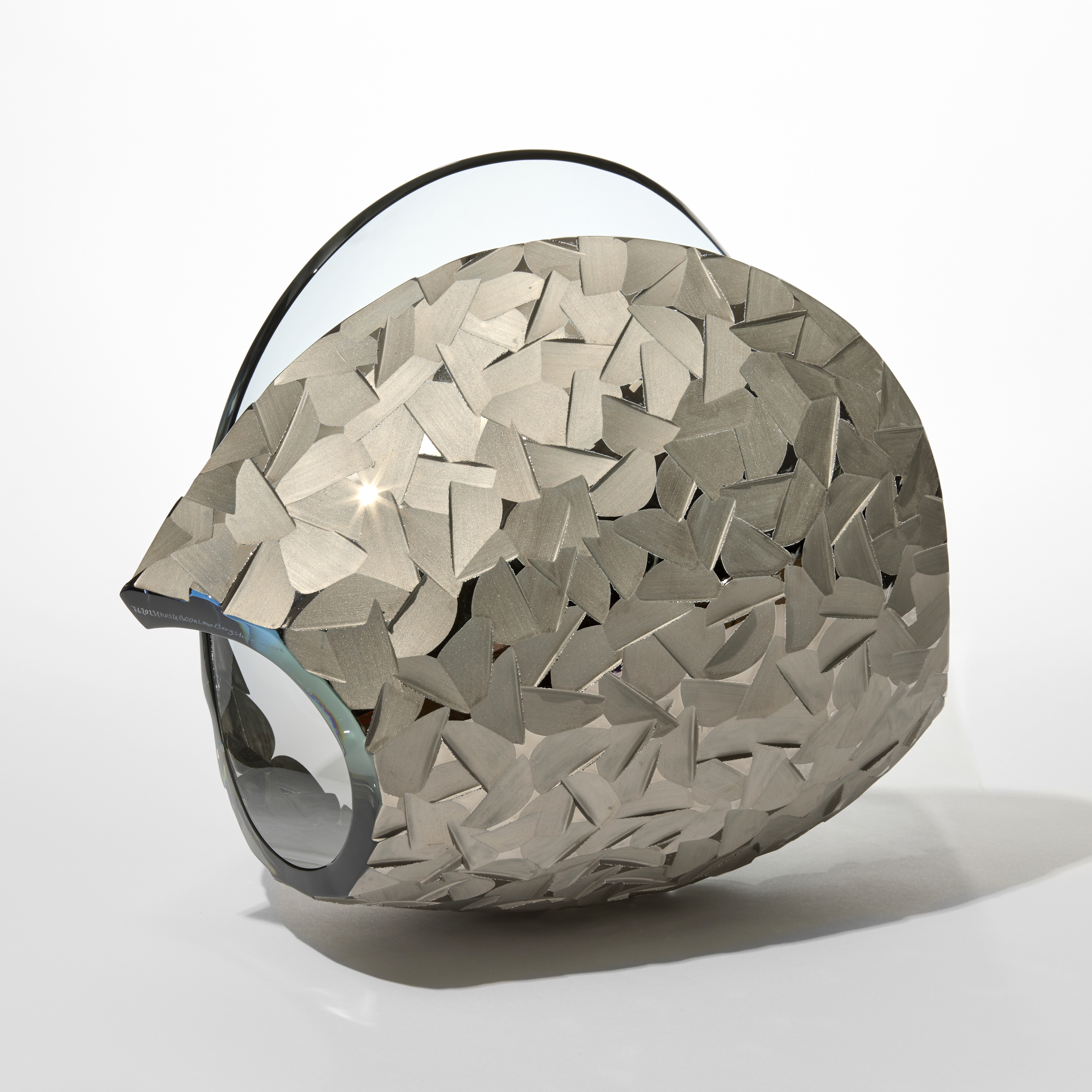 transparent curled simplified shell form in soft ice blue with one side covered in angled facets in matt platinum silver hand made and blown from glass and silver lustre