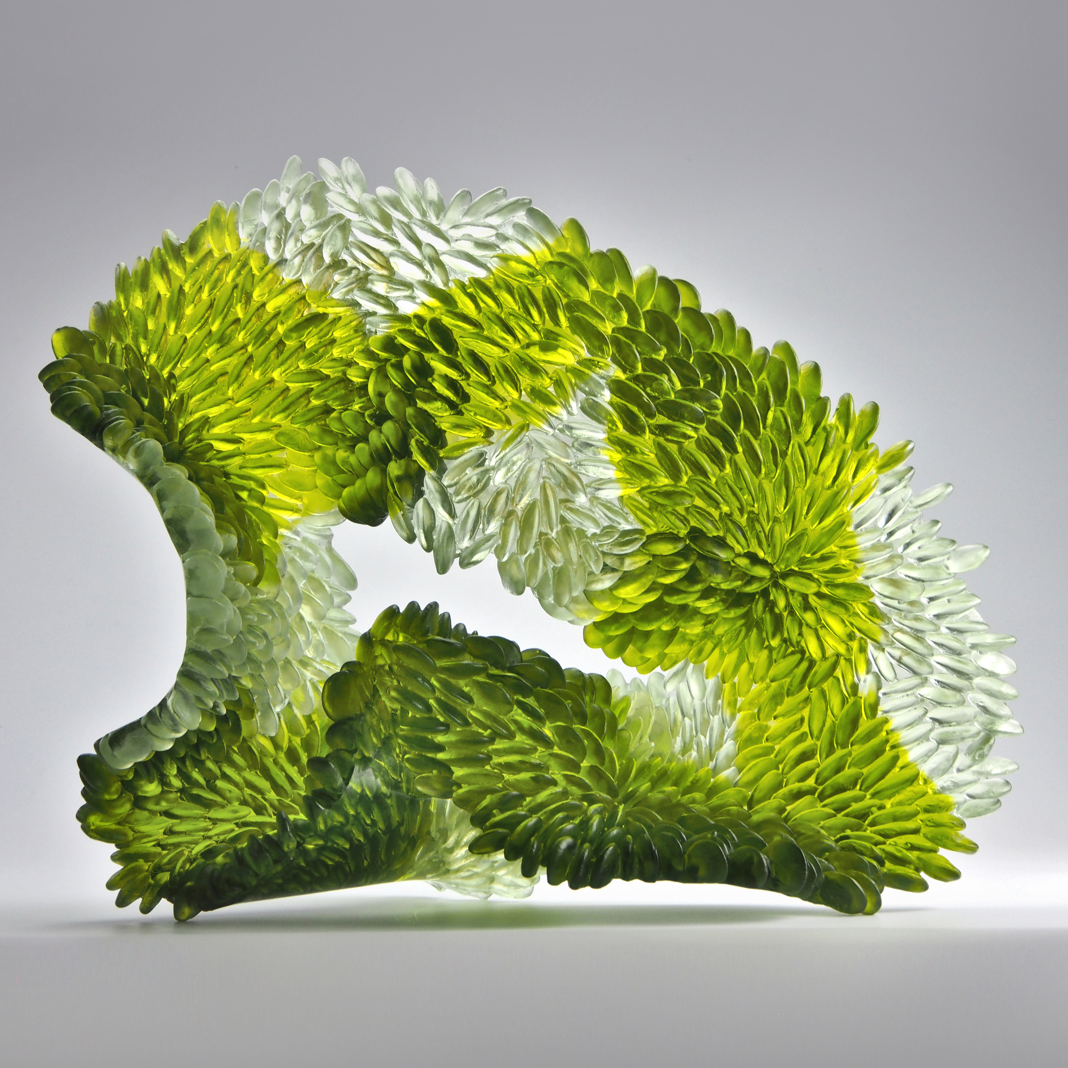 organic standing sculpture in olive green and clear with central gap and front face covered in raised half discs like scales made from cast glass