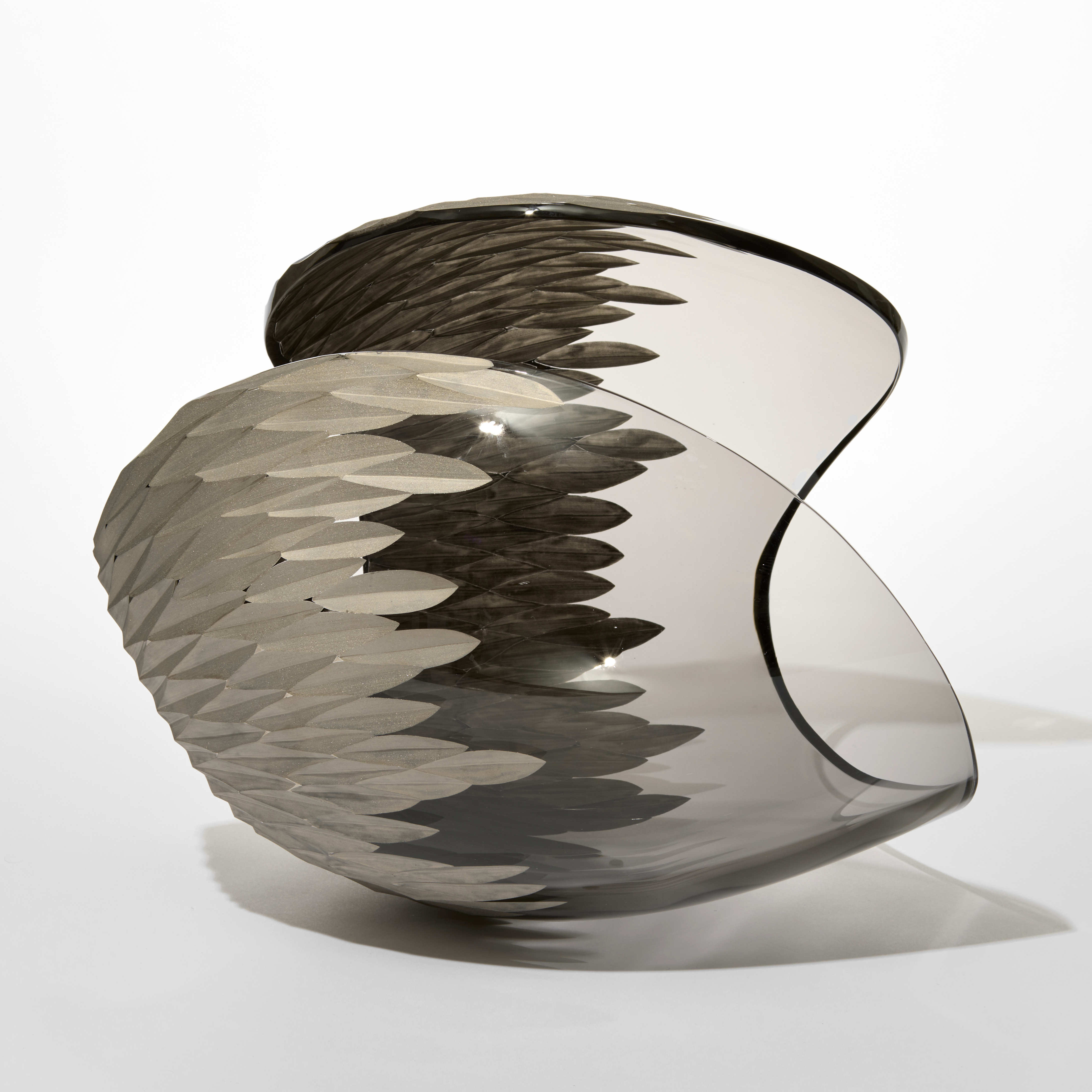 transparent dark grey rounded prone form with a large central section cut away on the top with one end covered in an incised repeat diamond pattern in matt silver hand blown from glass