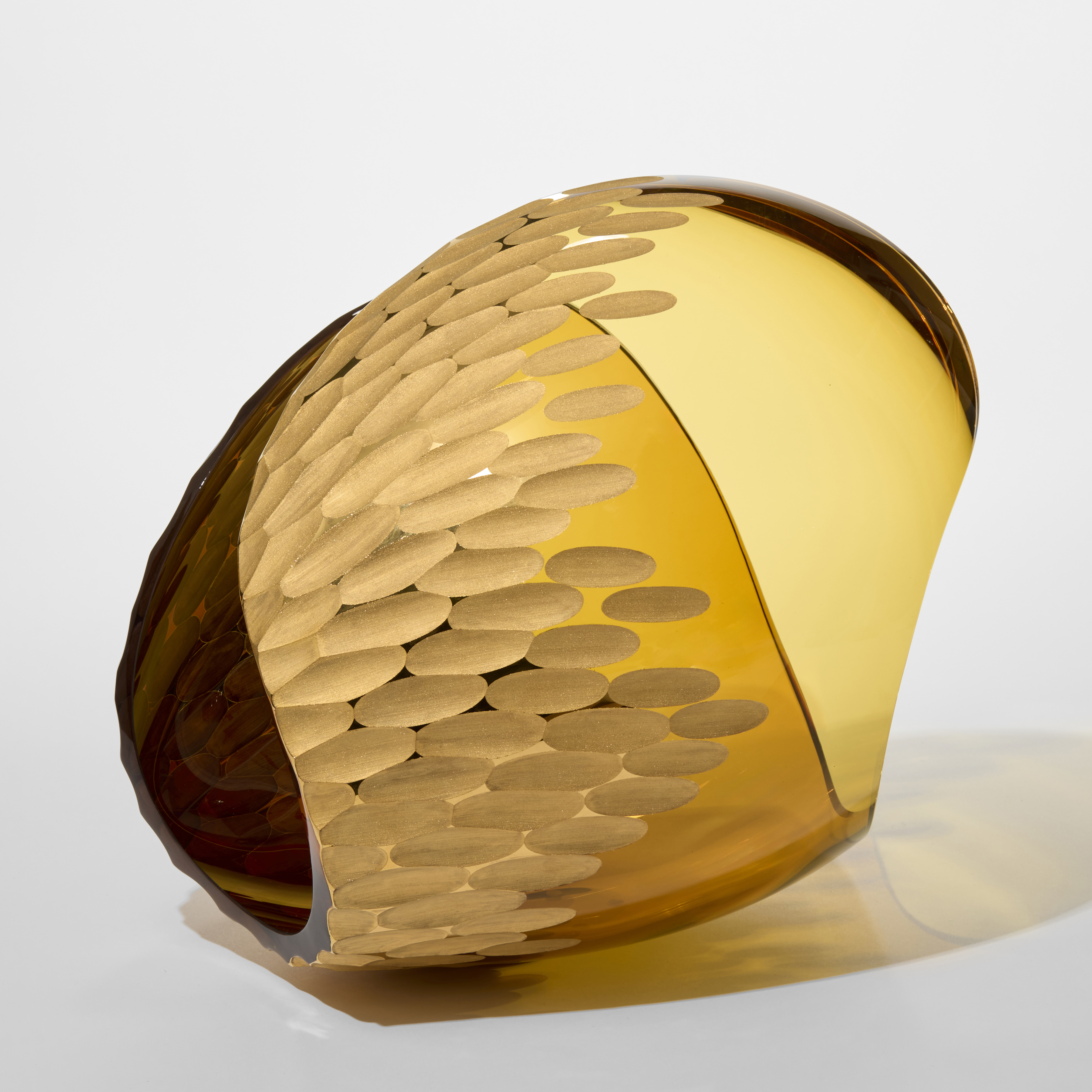 transparent amber curled form resembling a simplified conch shell with a clustered incised ovoid recessed repeat pattern cut into the outer surface hand blown from glass with twenty three carat gold 