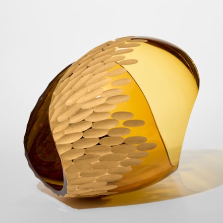 transparent amber curled form resembling a simplified conch shell with a clustered incised ovoid recessed repeat pattern cut into the outer surface hand blown from glass with twenty three carat gold