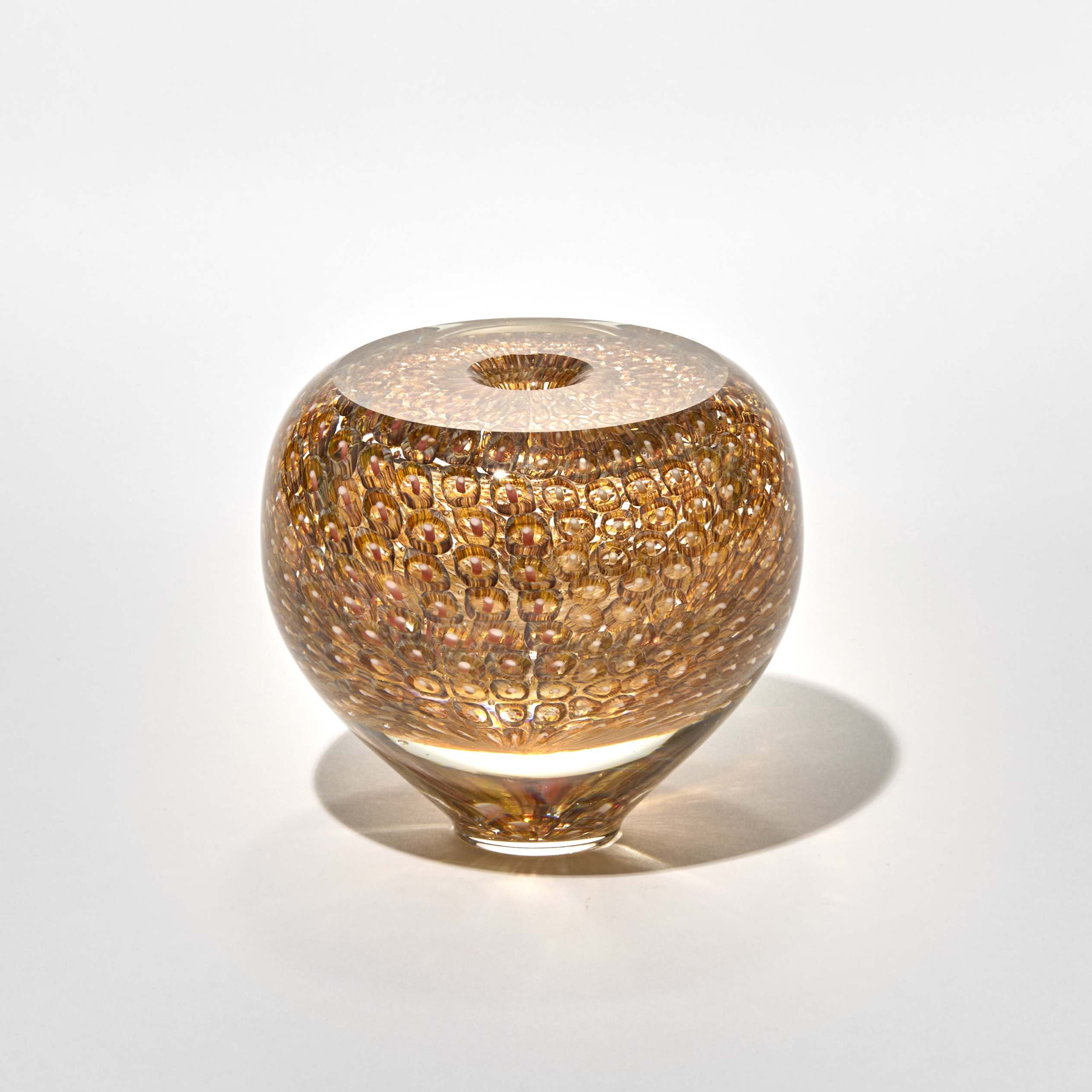 small rounded glass vase with a small top opening in golden amber with a narrow base and bulbous form and the smooth surface covered with a repeating honeycomb pattern of circular impressions giving it a luminous gem-like quality hand made from blown glass