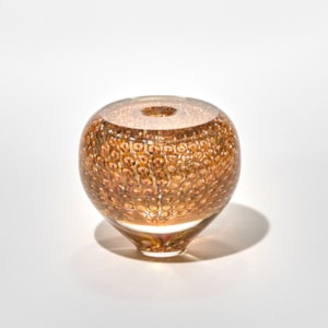 small rounded glass vase with a small top opening in golden amber with a narrow base and bulbous form and the smooth surface covered with a repeating honeycomb pattern of circular impressions giving it a luminous gem-like quality hand made from blown glass