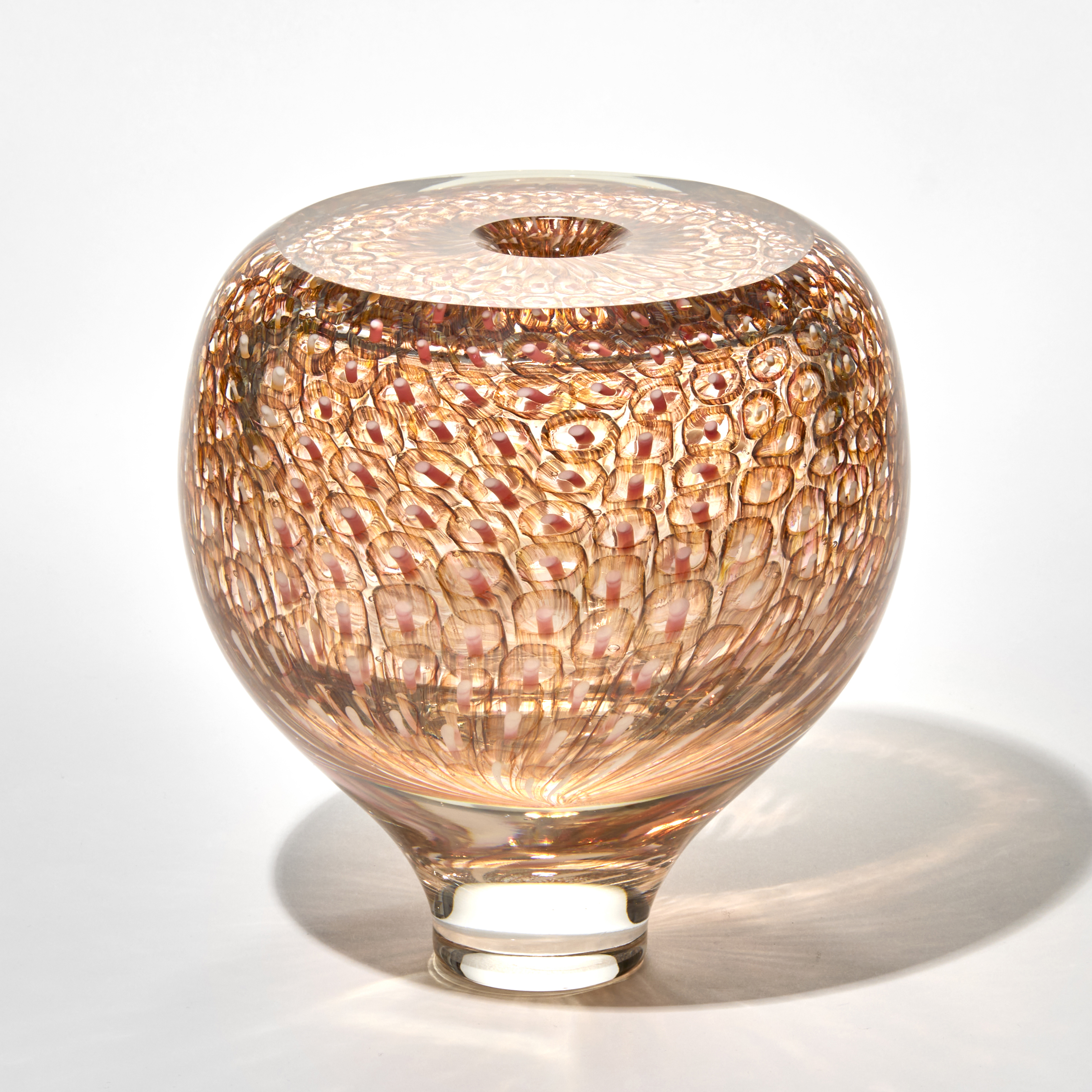 spherical glass vase with flat top surface and small opening in soft amber tones with a narrow clear base and the surface decorated with a repeating honeycomb pattern of circular impressions hand made from blown glass