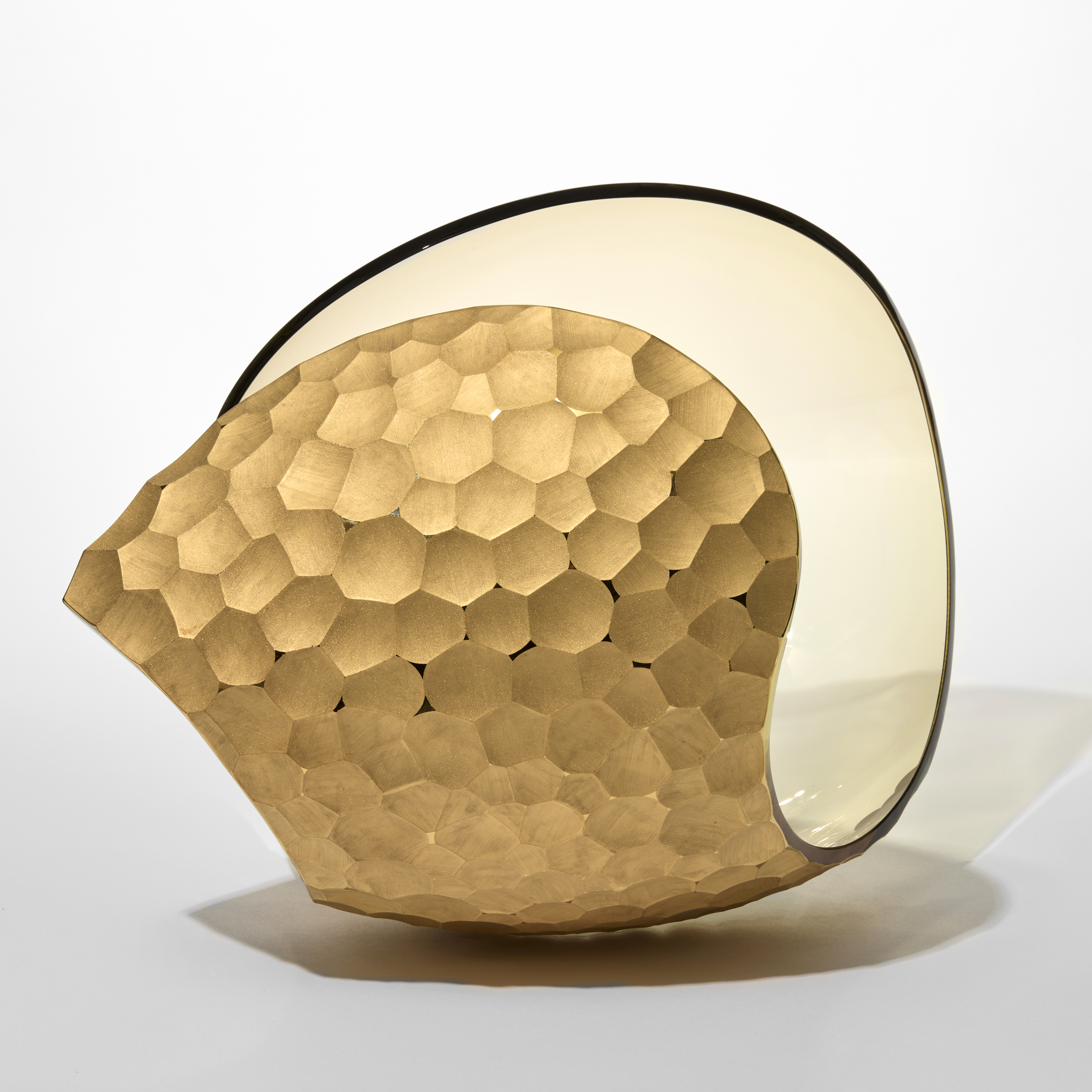 curled shell like form in transparent soft amber with one side covered in repeat cut scalloped recesses hand blown from glass with a twenty three carat gold finish 