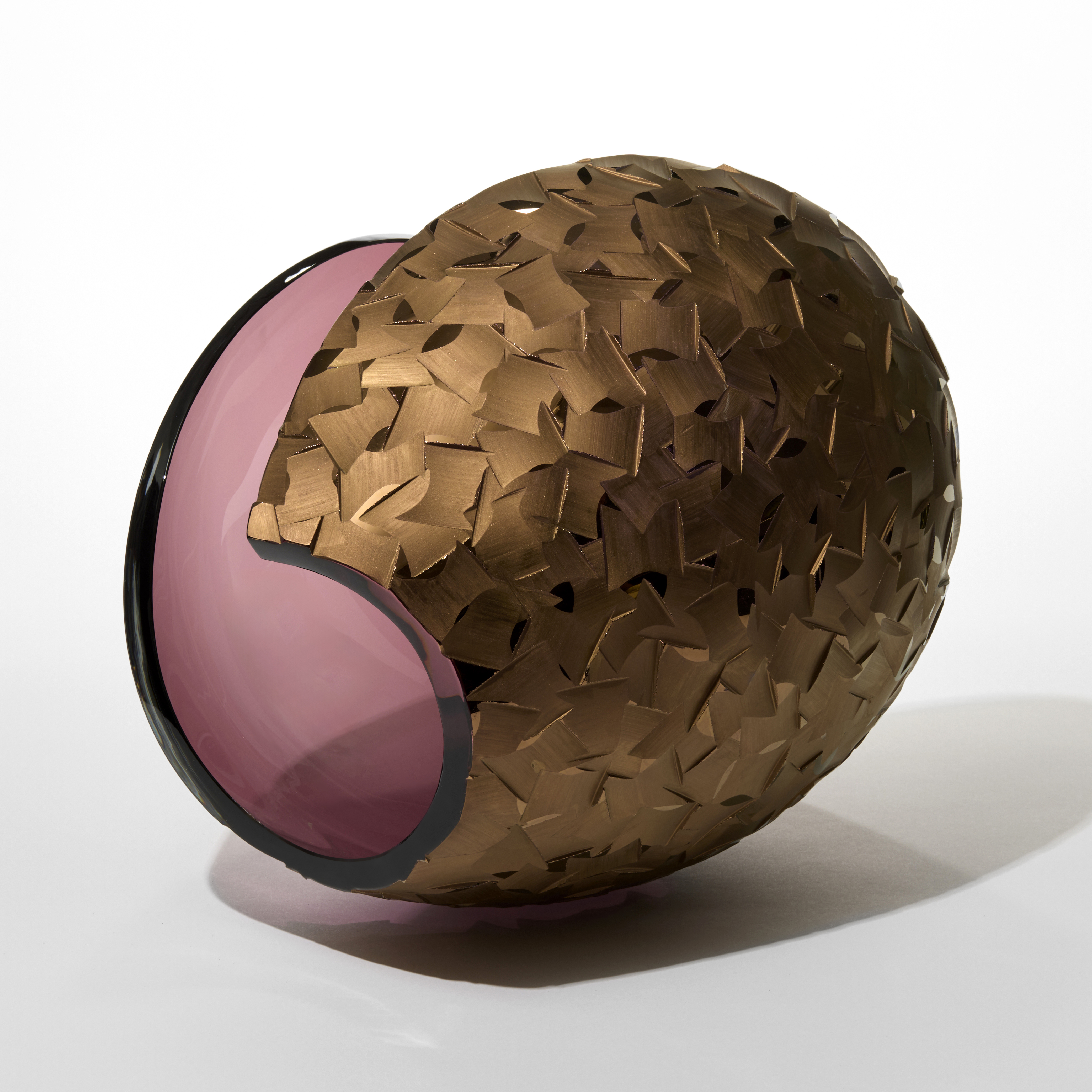 curled egg shaped form in transparent aubergine with one side glossy and the other incised and cut into in with a repeat tessellated pattern hand blown from glass with a matt twenty three carat gold finish
