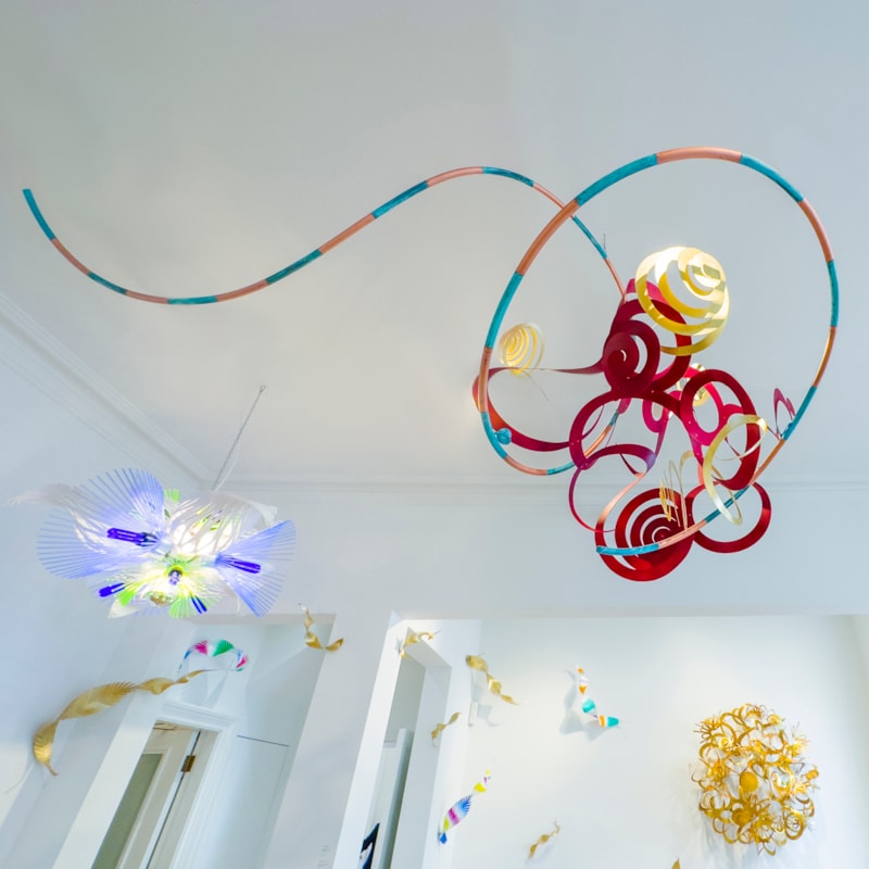 red gold aqua and copper hanging sculpture consisting of a mass of swirls curls and spirals created from flat sheet metal and twisted into three dimensional forms created from hand-painted copper, oxydyed aluminium & brass with a long trailing striped tail like a kite