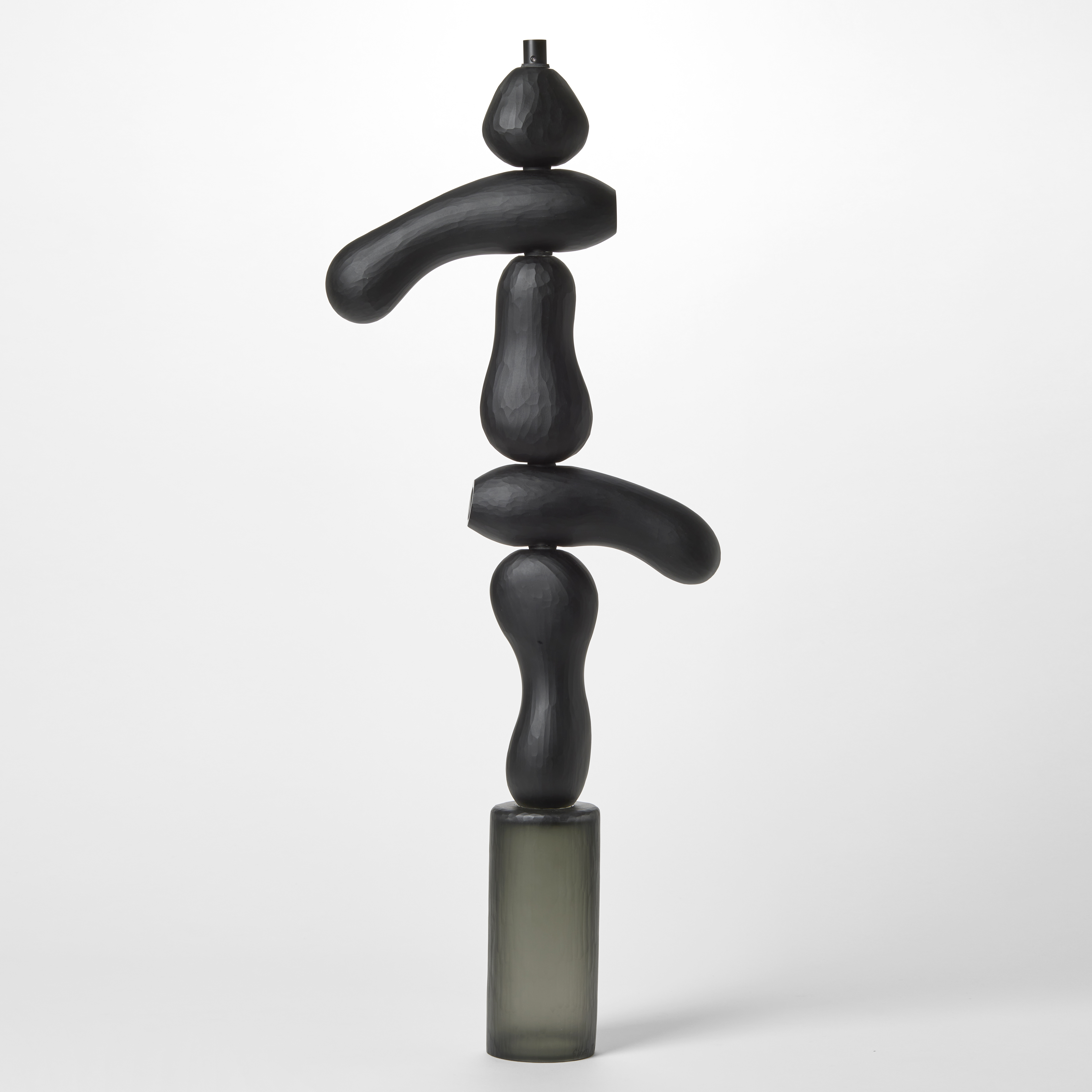 tall totem inspired sculpture with stacked geometric shapes in dense black with a cylindrical base in opaque grey hand made from blown glass with a repeat textured cut surface