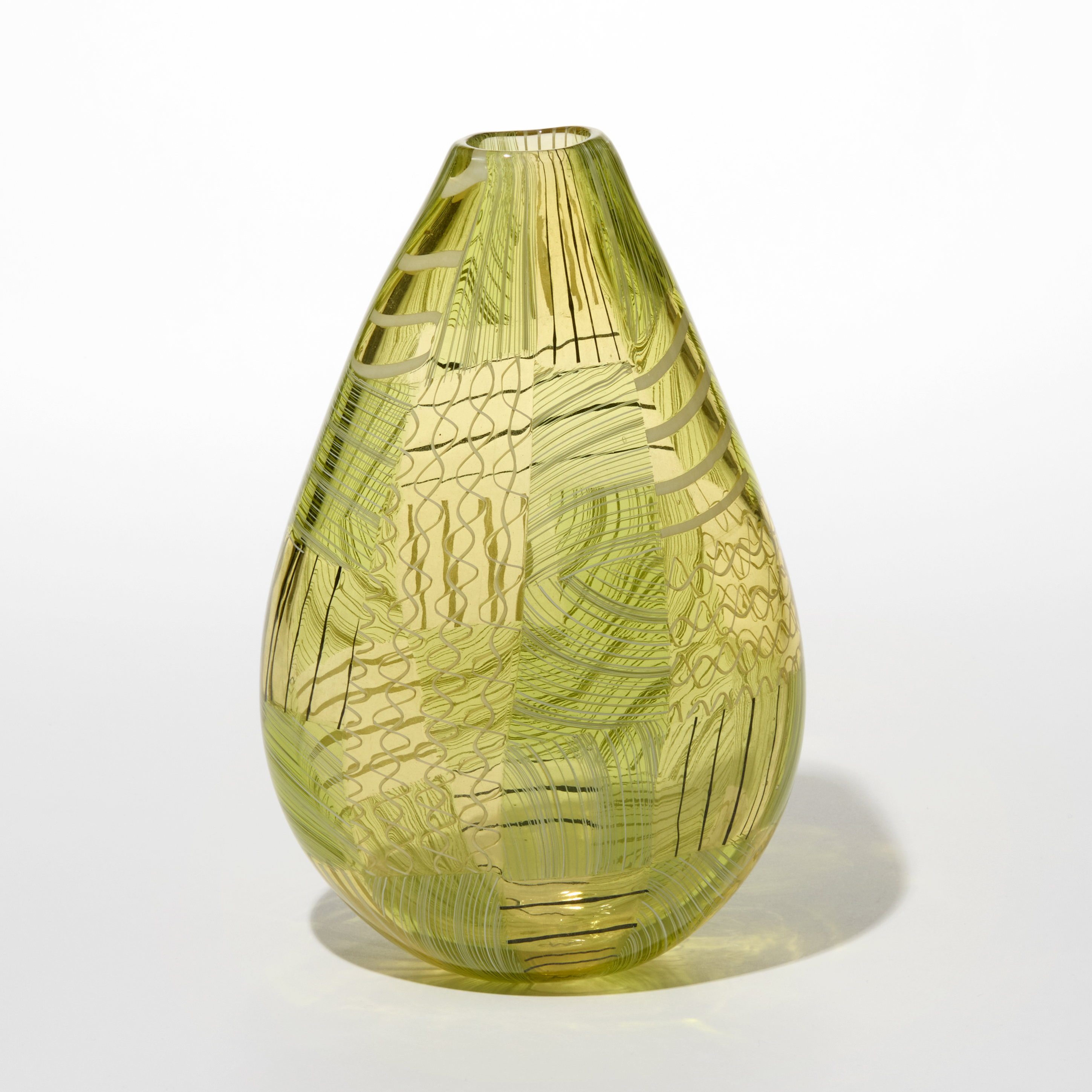 decorative teardrop shaped transparent vase with a narrow top opening in a translucent greenish yellow hue with layered intricate geometric patterns in cross hatches and flowing lines overlapping each other and crisscrossing in streaks of darker and lighter shades of green hand made from blown glass