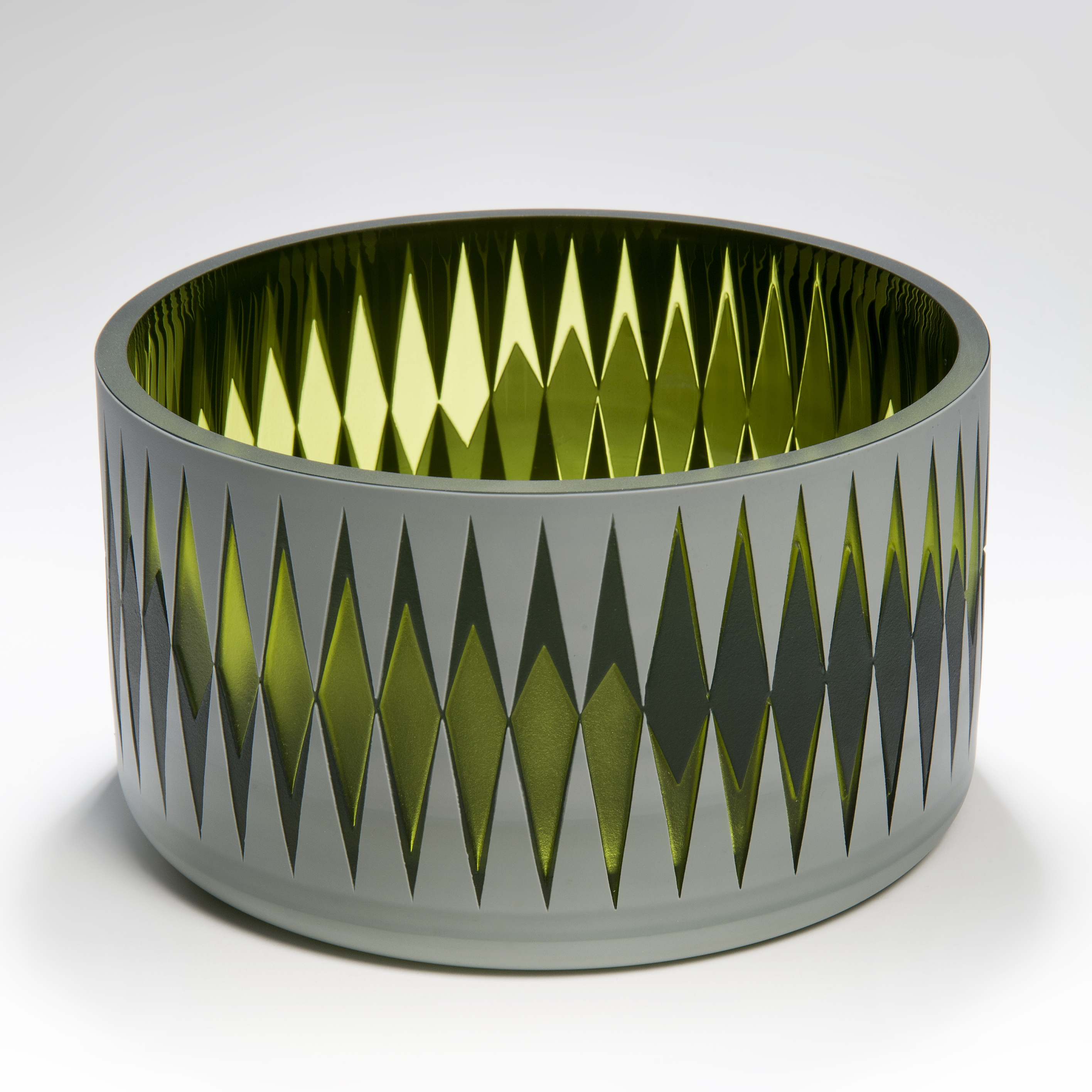 low round vessel with an opaque grey surface and a diamond pattern travelling right around the piece revealing further shapes increasing and decreasing in size in black and transparent green hand made from blown glass