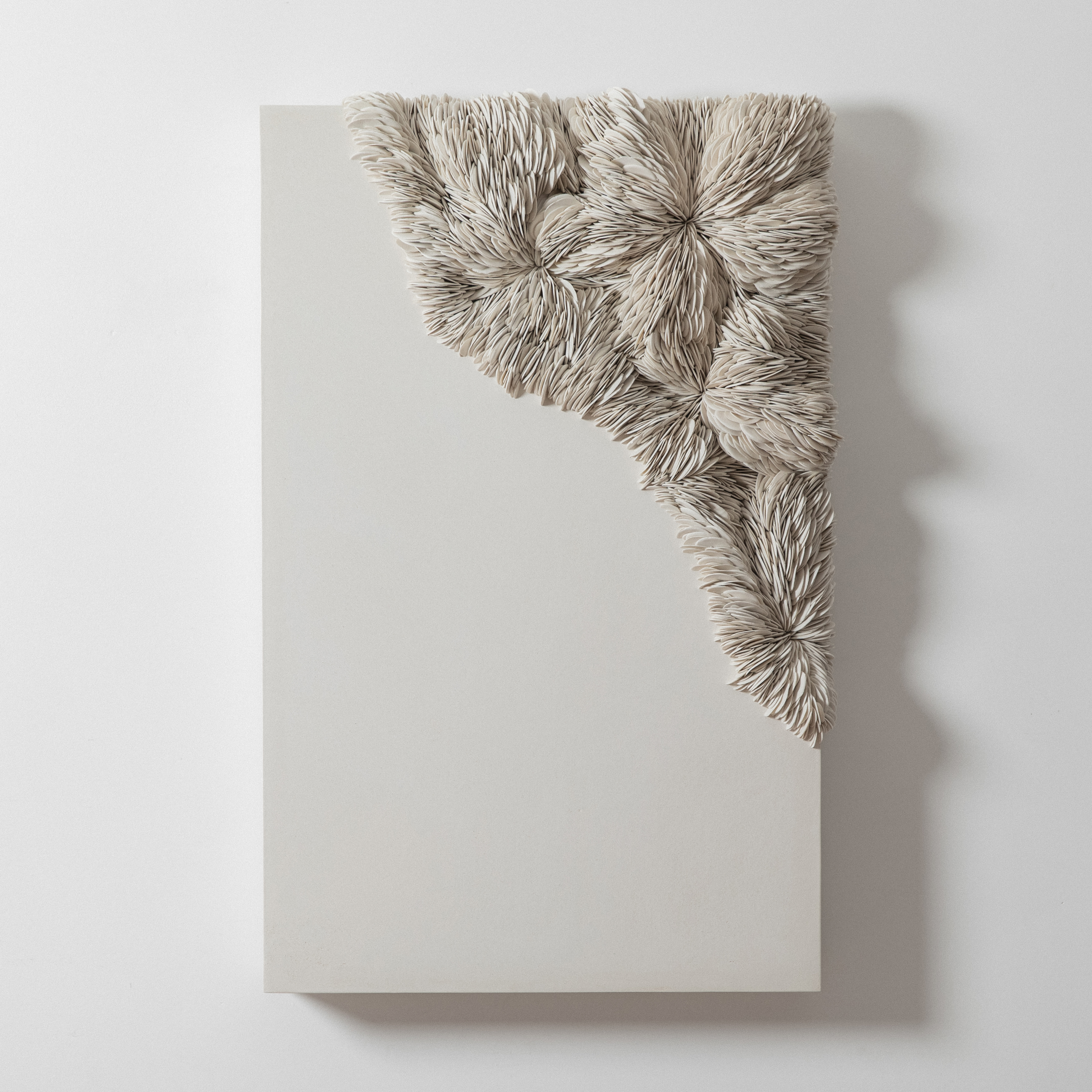 a large white wall mounted artwork consisting of a single thick slab in white with the top right hand corner embedded with hundreds of stacked and interlocking shards hand made from porcelain and tadelakt plaster