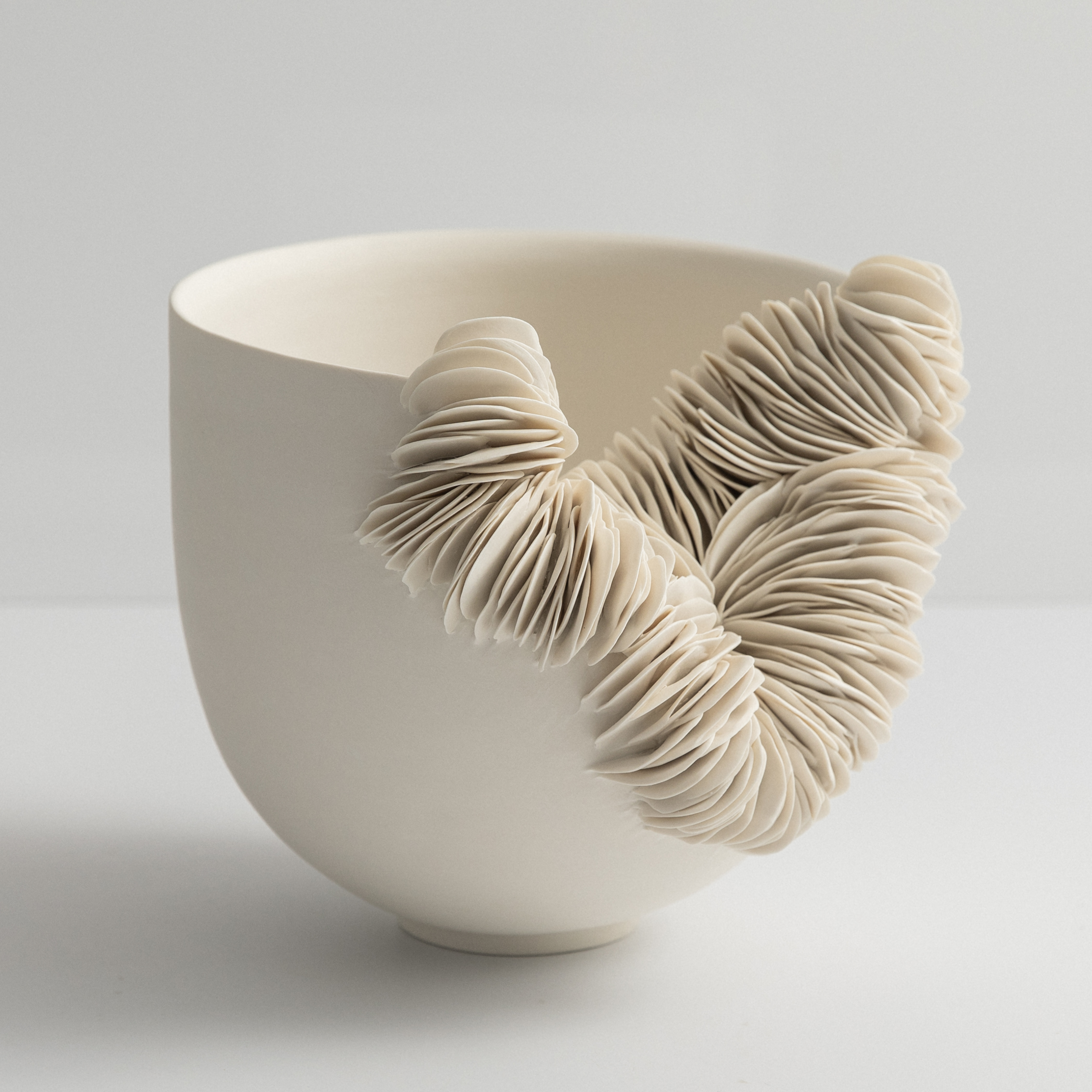 low wide round bowl in off white with the front third cut away and the gap filled with stacked shards hand made and thrown from porcelain