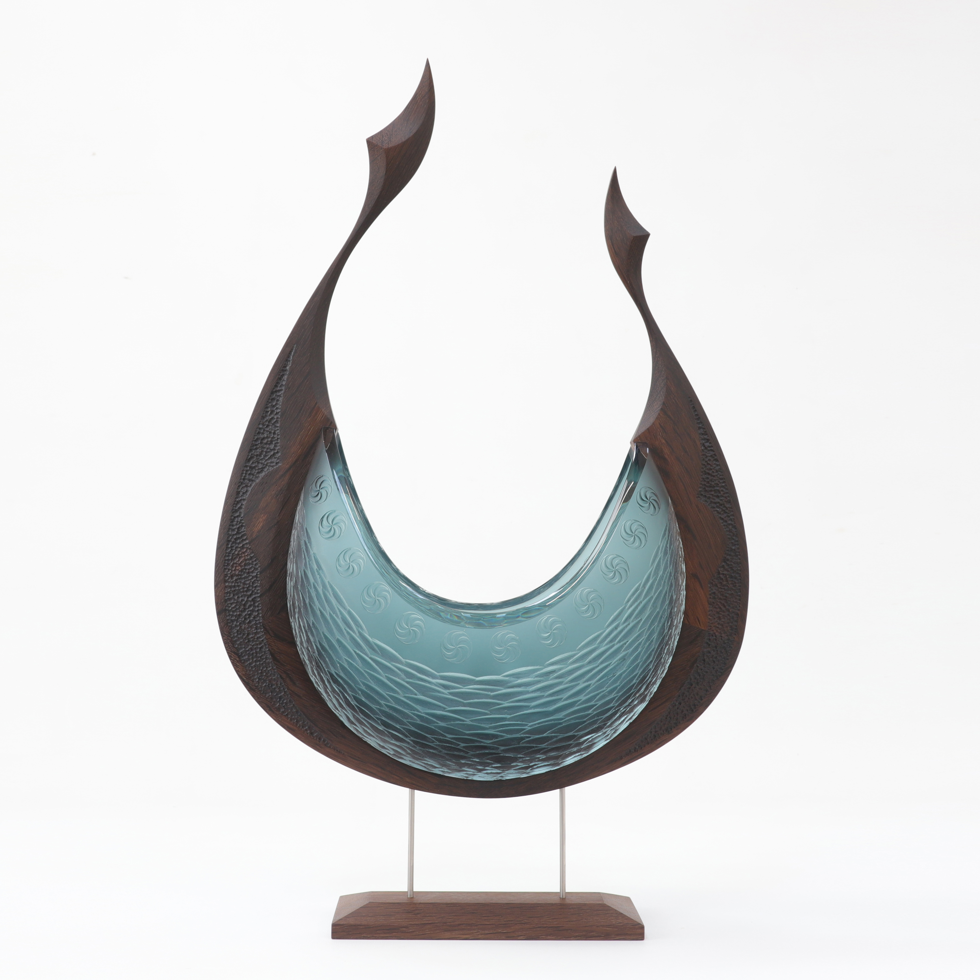 stylised viking ship artwork with dramatically curved oak keel with pointed fin shaped finials and hull made from blown and pattern cut glass in steel blue sat perched on a steel and oak stand
