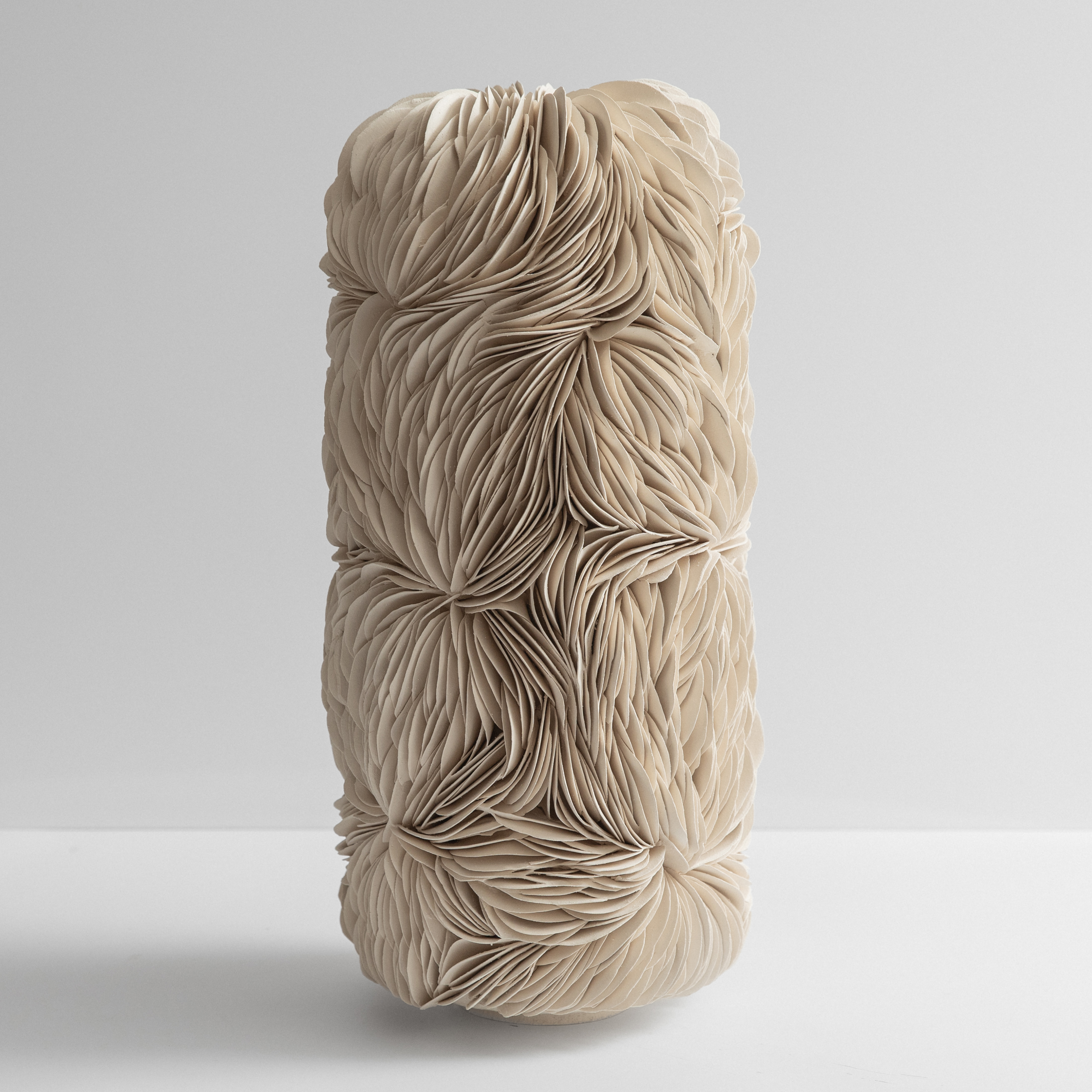 standing wide column form with a domed top and small top opening completely covered in interlocking curved off white shards of ceramic hand made from stoneware clay