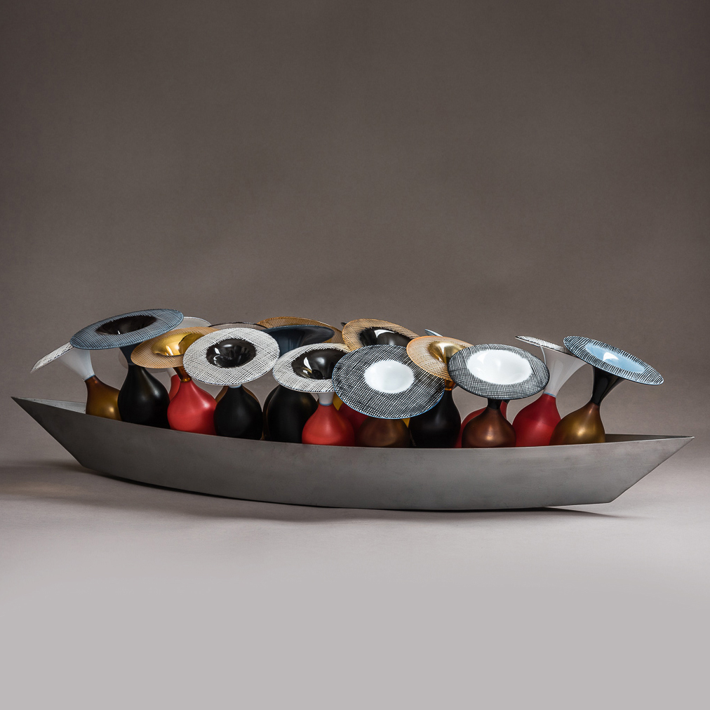 long angular matt silver metal hull containing opaque amphora bottles in gold red and purple each with wide flaring rims with cross hatched patterns in black and white on the top hand blown from glass