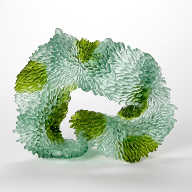 standing abstract looping and undulating sculpture in opaque jade and emerald green with the front surface covered in small raised scales hand made from cast glass
