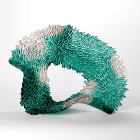 standing looped abstract sculpture in opaque teal green with patches of grey with the front surface covered in small repeat raised discs like scales hand made from cast and sculpted glass