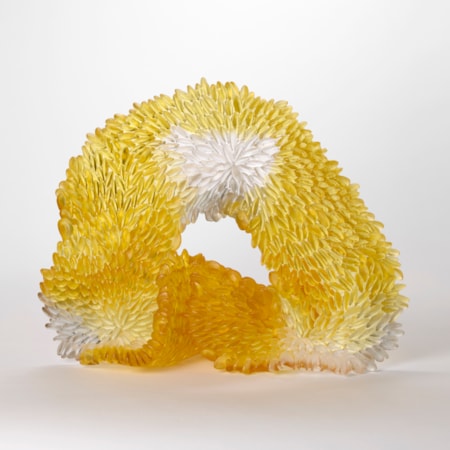 standing soft sagging opaque looped abstract sculpture in brilliant amber gold with patches of grey and white with the front surface covered in raised scales hand made from glass