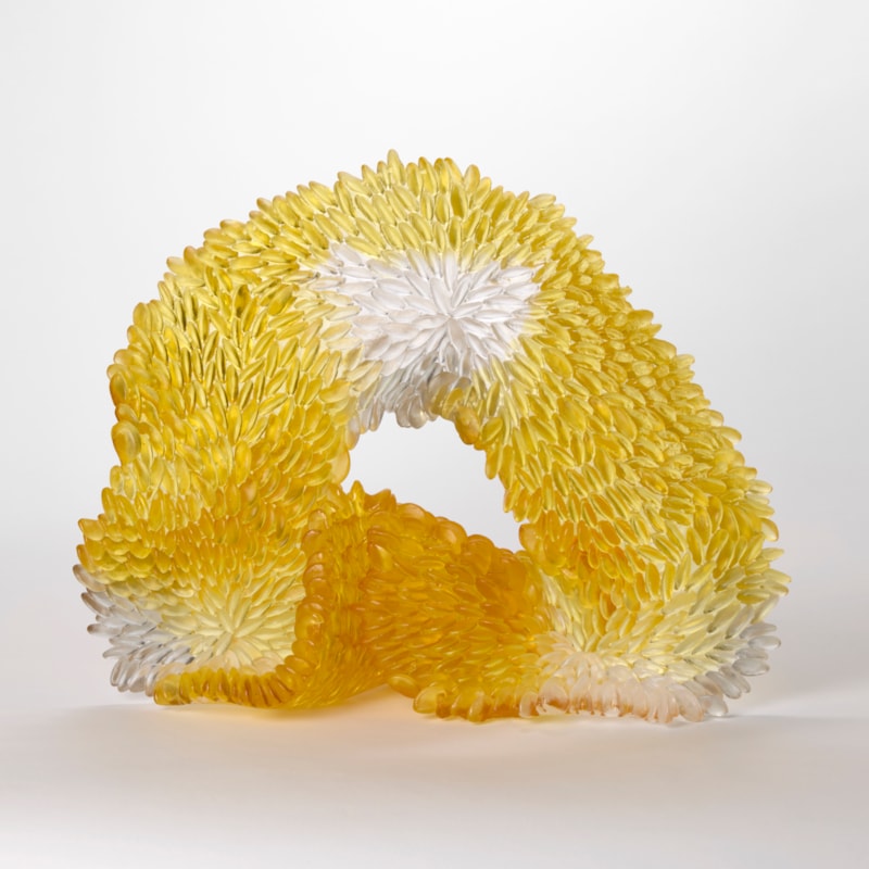 standing soft sagging opaque looped abstract sculpture in brilliant amber gold with patches of grey and white with the front surface covered in raised scales hand made from glass