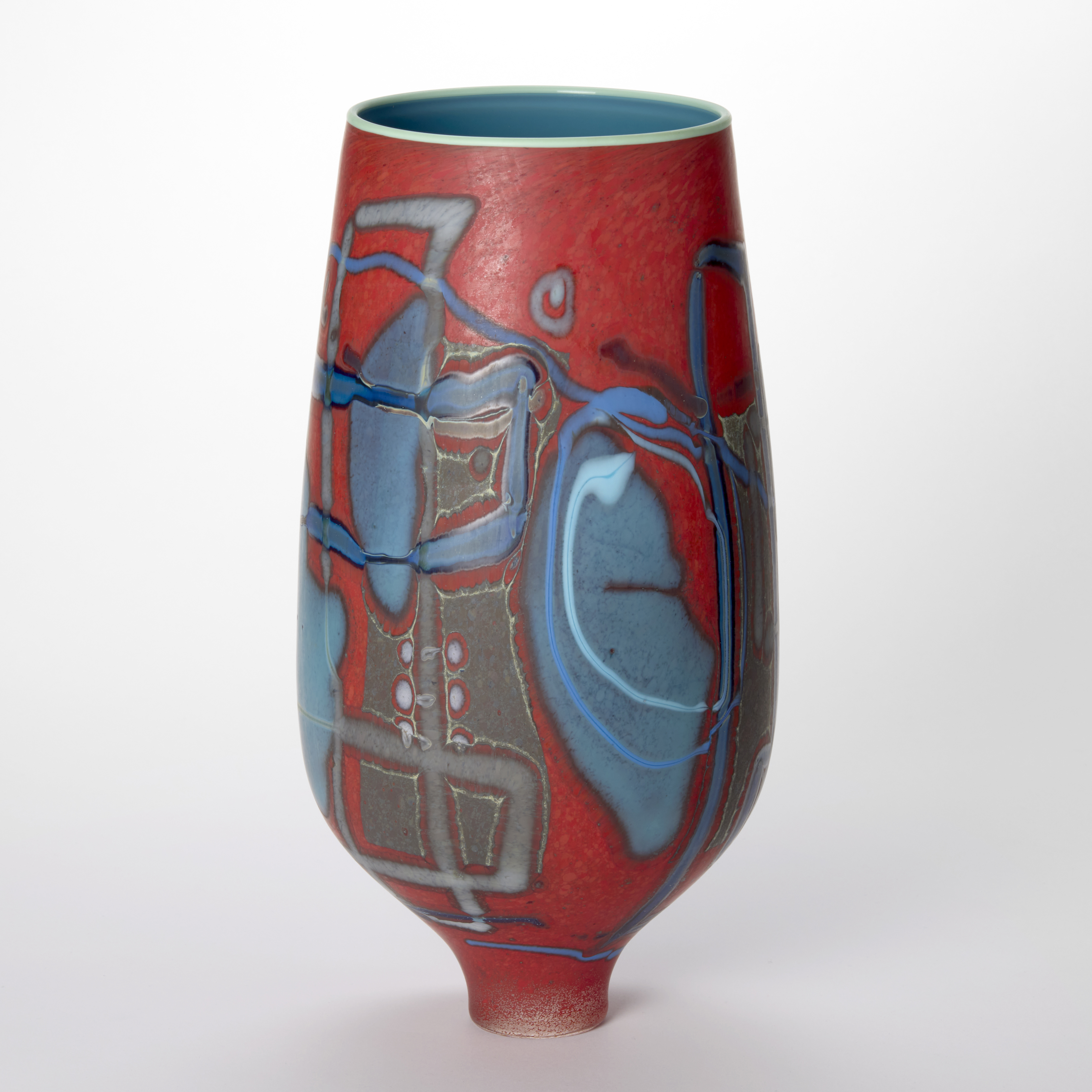 tall matt red vase with a bulbous shape tapering to an elegant narrow foot with the surface covered in abstract patterns and shapes in various hues of blue with a wide top opening with a narrow rim in aquamarine and an interior in glossy denim blue hand made from glass 