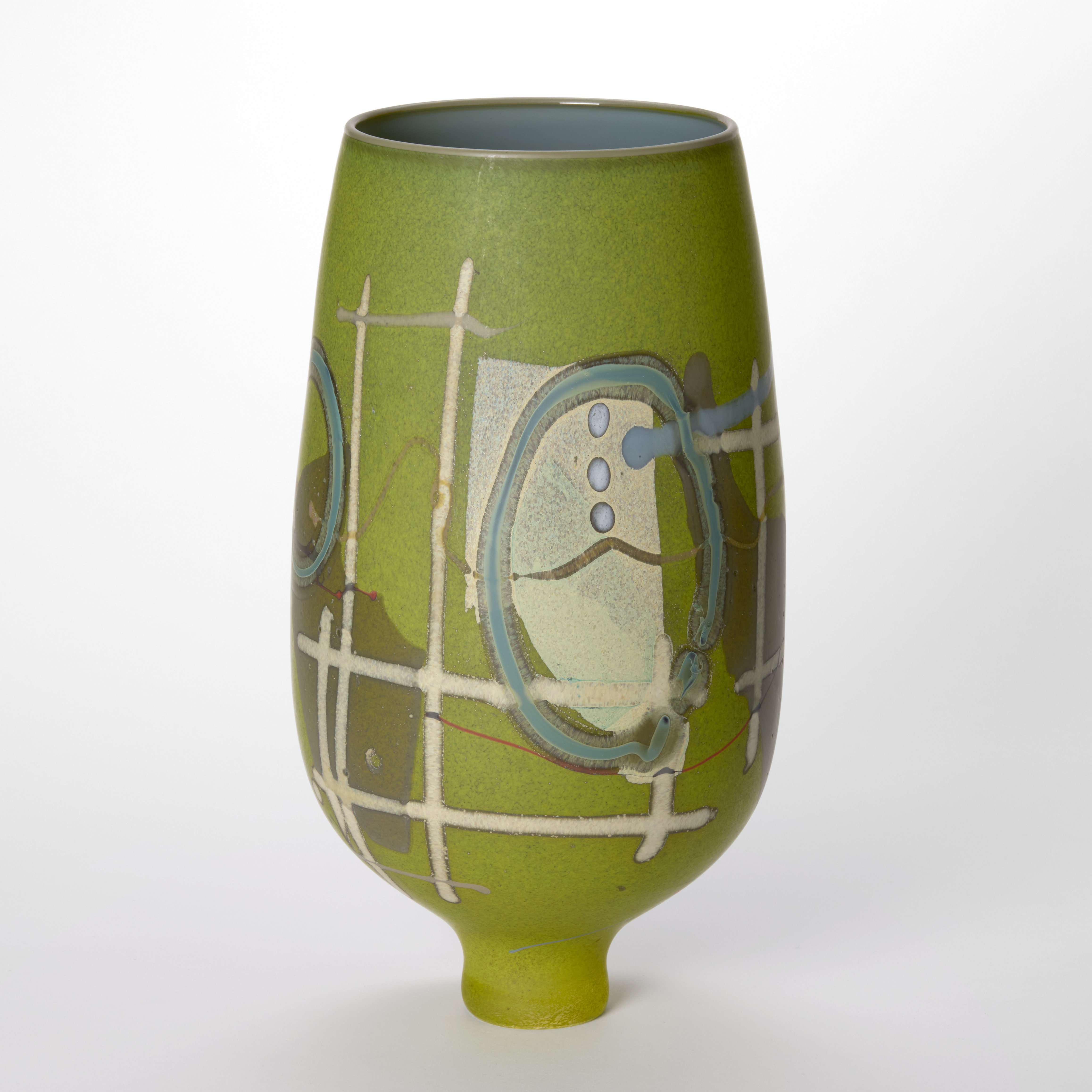 tall round matt lime green vase perched on a tapering small foot with the surface covered in abstract patterns and motifs in beige teal brown and soft pink with a glossy denim blue interior hand made from blown glass