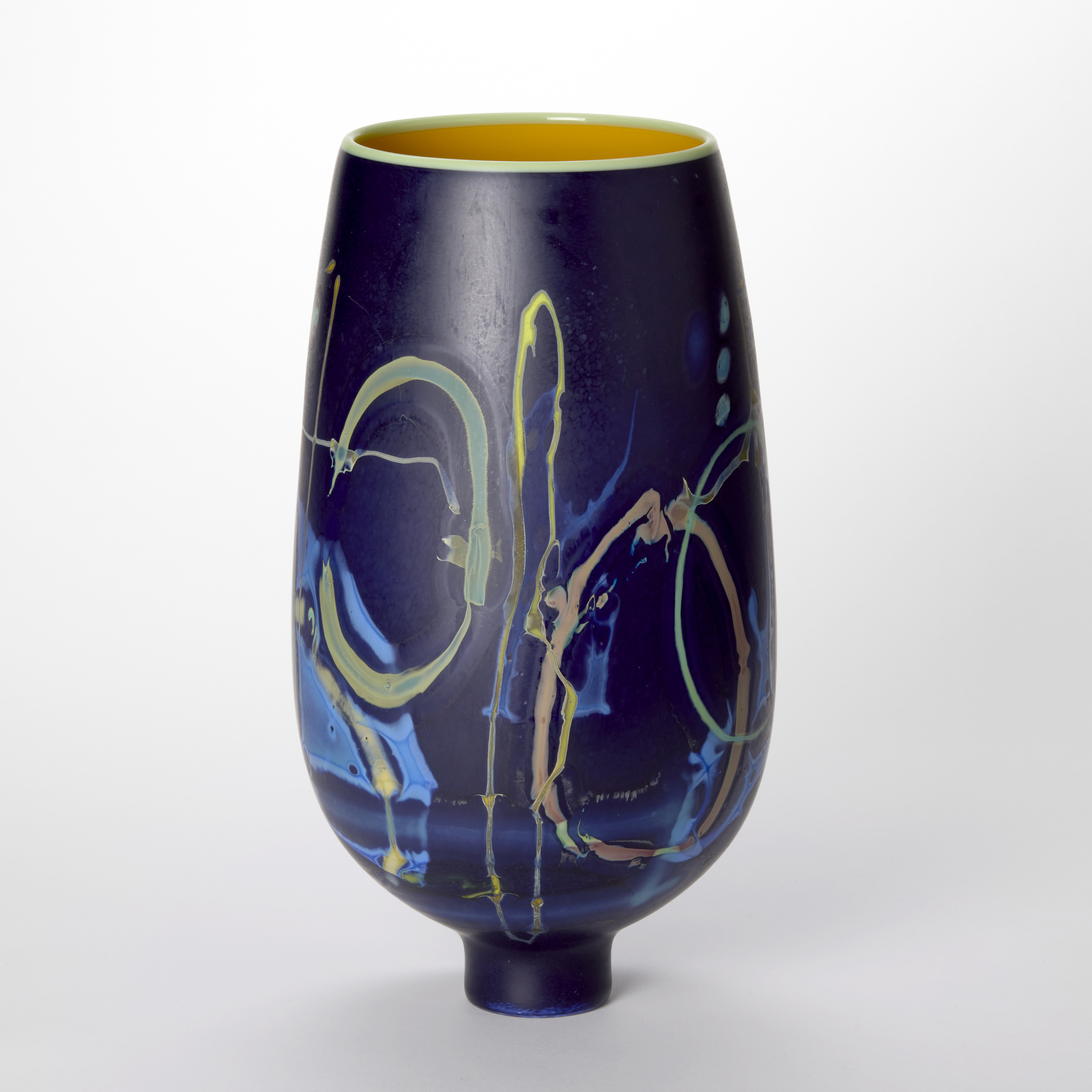 round bulbous vase tapering to a narrow foot in rich deep purple blue with surface meandering line abstract patterns in yellow mint blue and soft pink with a glossy interior in egg yolk yellow and a wide opening with a rim in citrus yellow hand made from blown glass