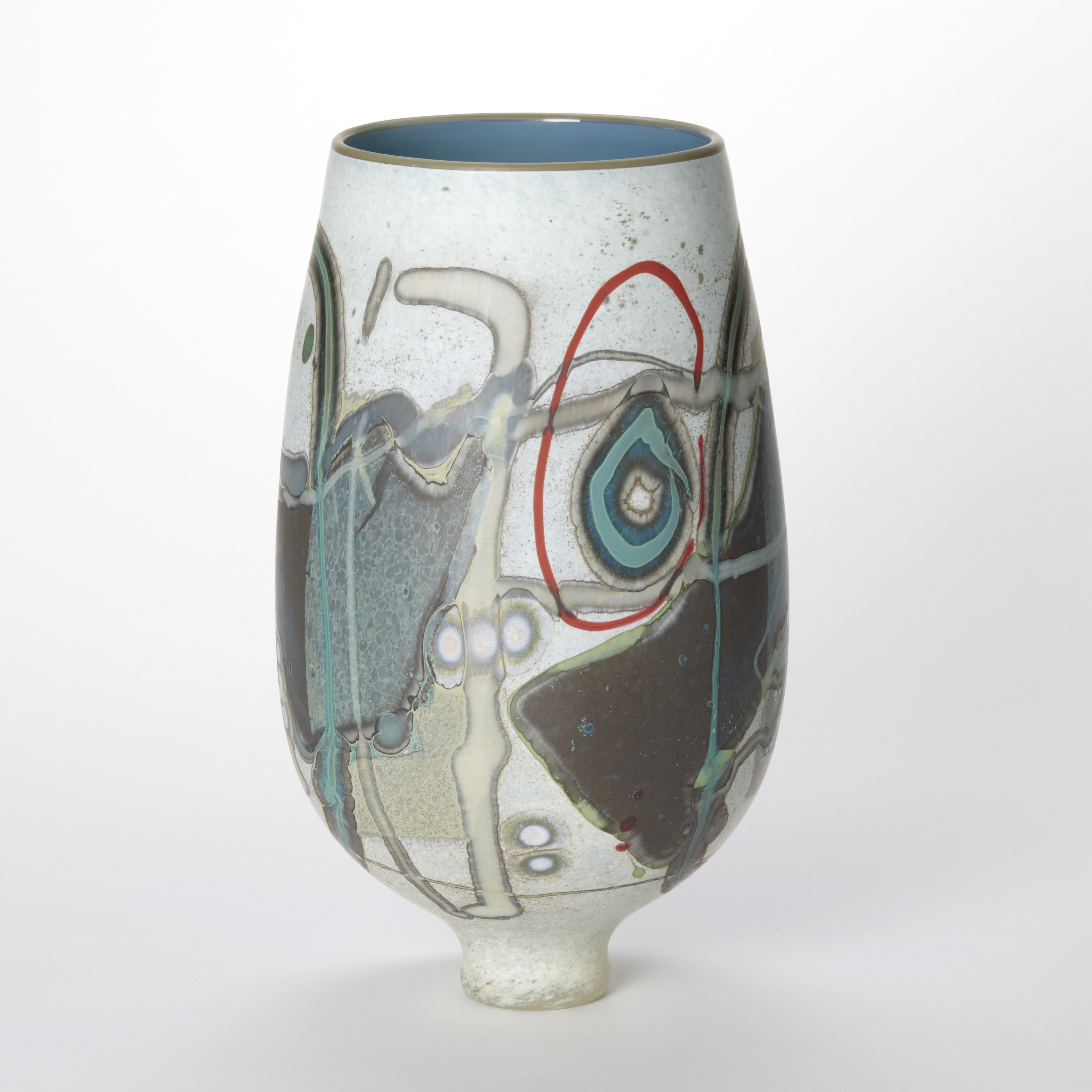 round teardrop shaped vase with wide opening and small foot in opaque mottled white covered in abstract linear and circular patterns in chocolate teal beige and red with a shiny interior in duck egg blue with a thin olive green rim hand blown and sculpted from glass 