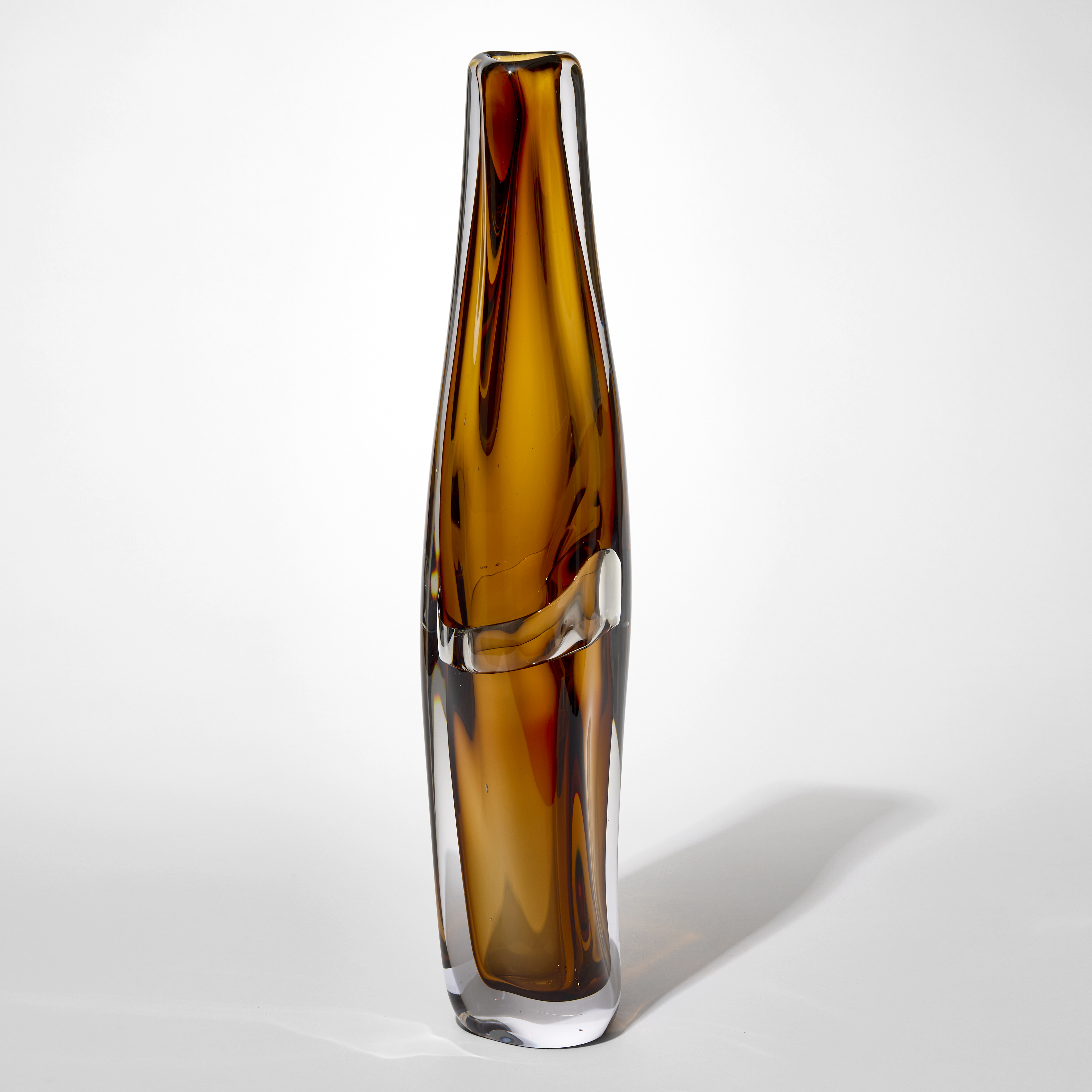 tall transparent slightly twisting vase with small top opening and layers in clear and amber brown with an undulating central belted section hand blown from glass