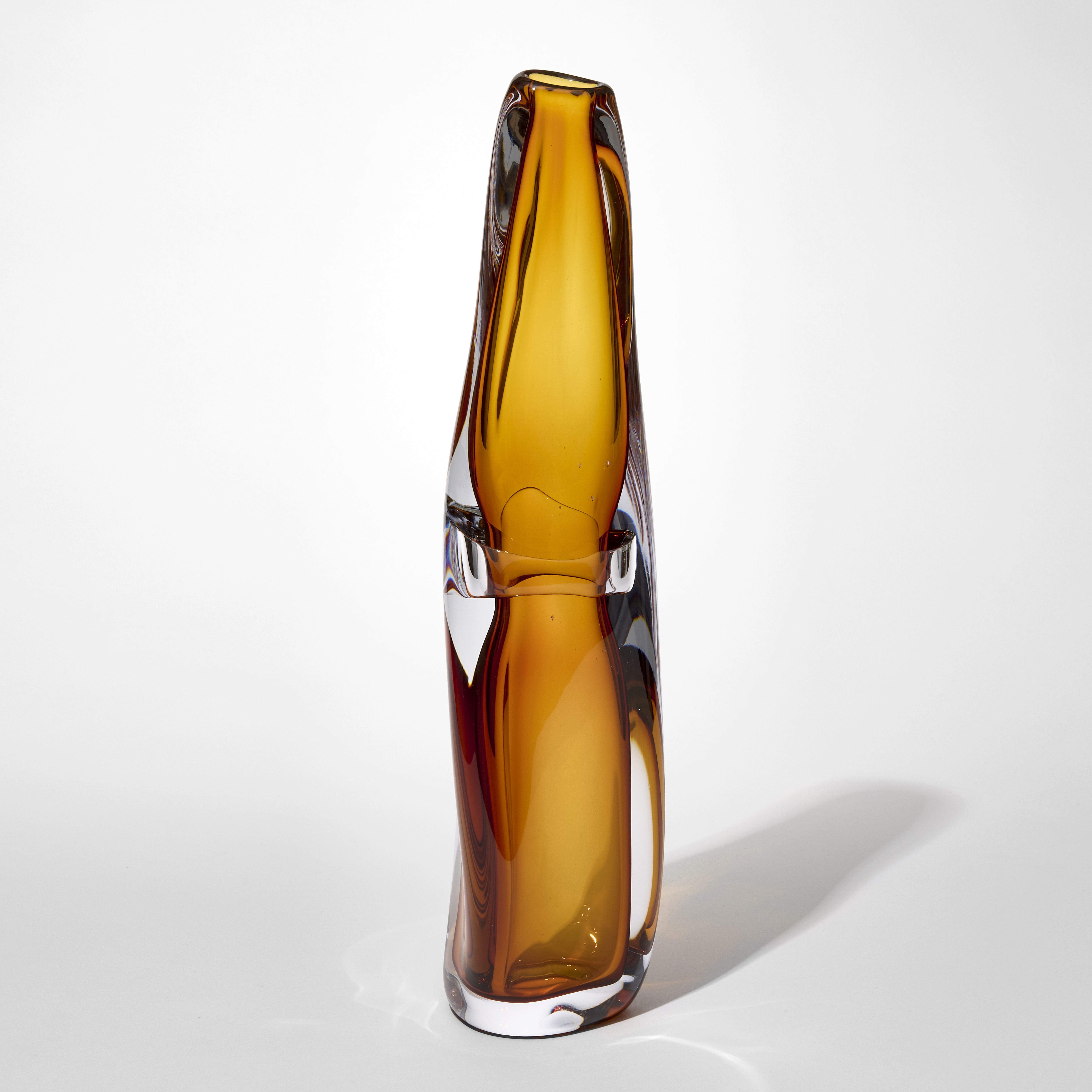 tall fluid transparent soft vase with an outer later in clear and inner trapped layer with a pinched waste in rich amber hand blown from glass