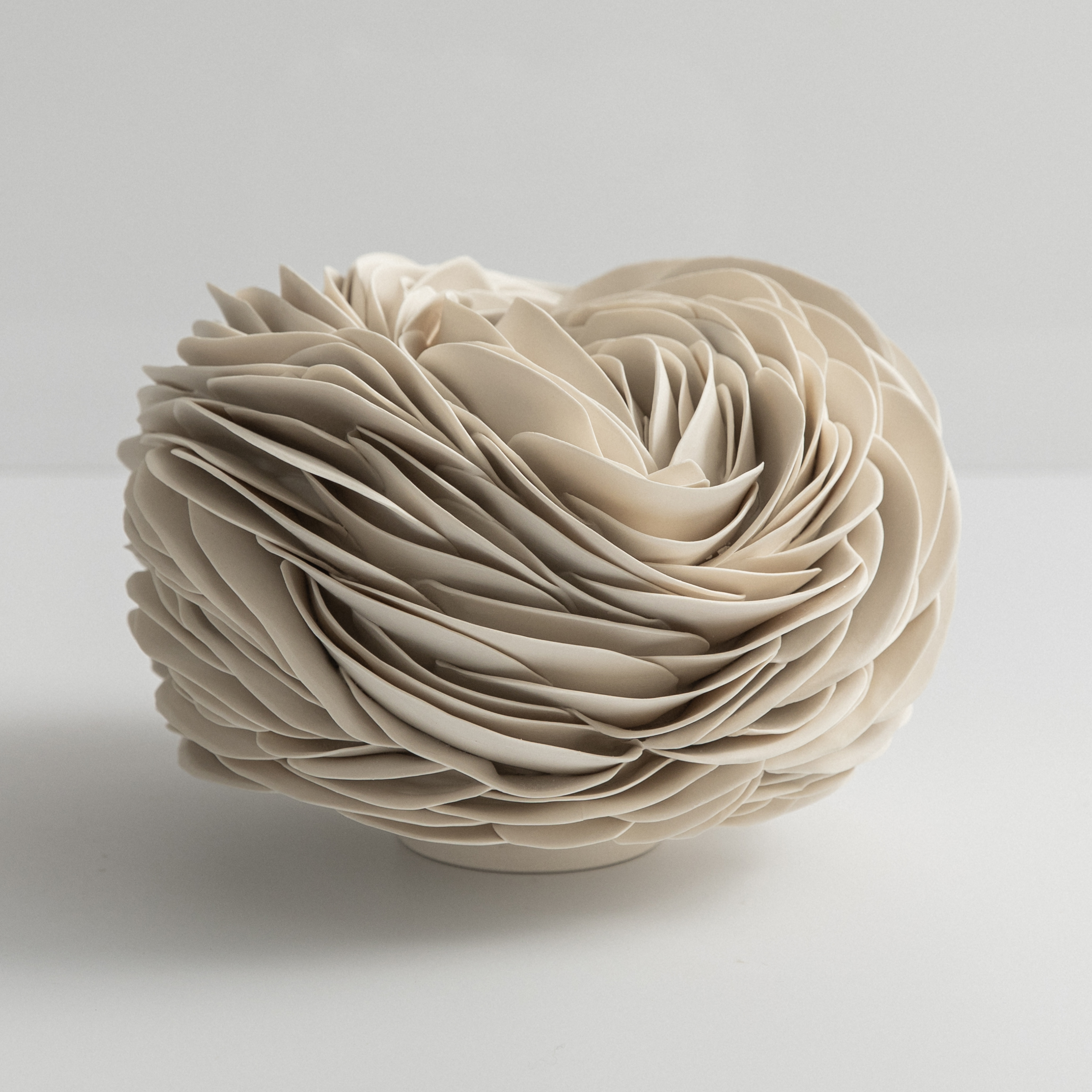 round low vessel form with a small top opening and the exterior covered in curved interwoven shards hand made from porcelain