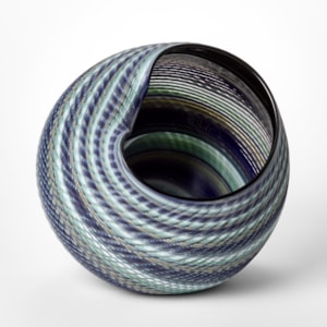large round matt woven basket shaped vessel with wide offset opening created from banded canes in indigo jade blue celadon and soft grey hand blown and cut from glass